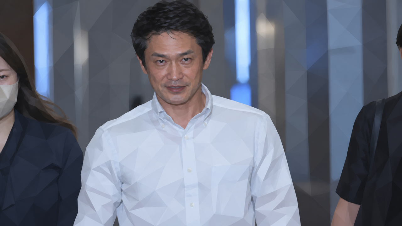 흰 셔츠를 입은 오가와 준야가 동행인들과 실내 복도를 지나고 있다.